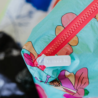 Closeup of Wings Hawaii foldable Tyvek adventure tote in kokio hibiscus print. Zipper detail says WINGS HI
