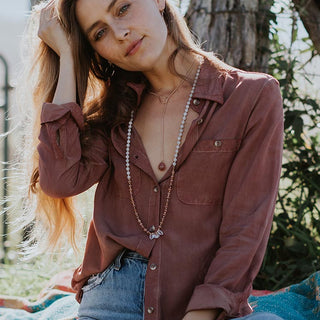 model wearing long beaded crystal necklace, lariat necklace with a sunstone and purple button up blouse and jeans